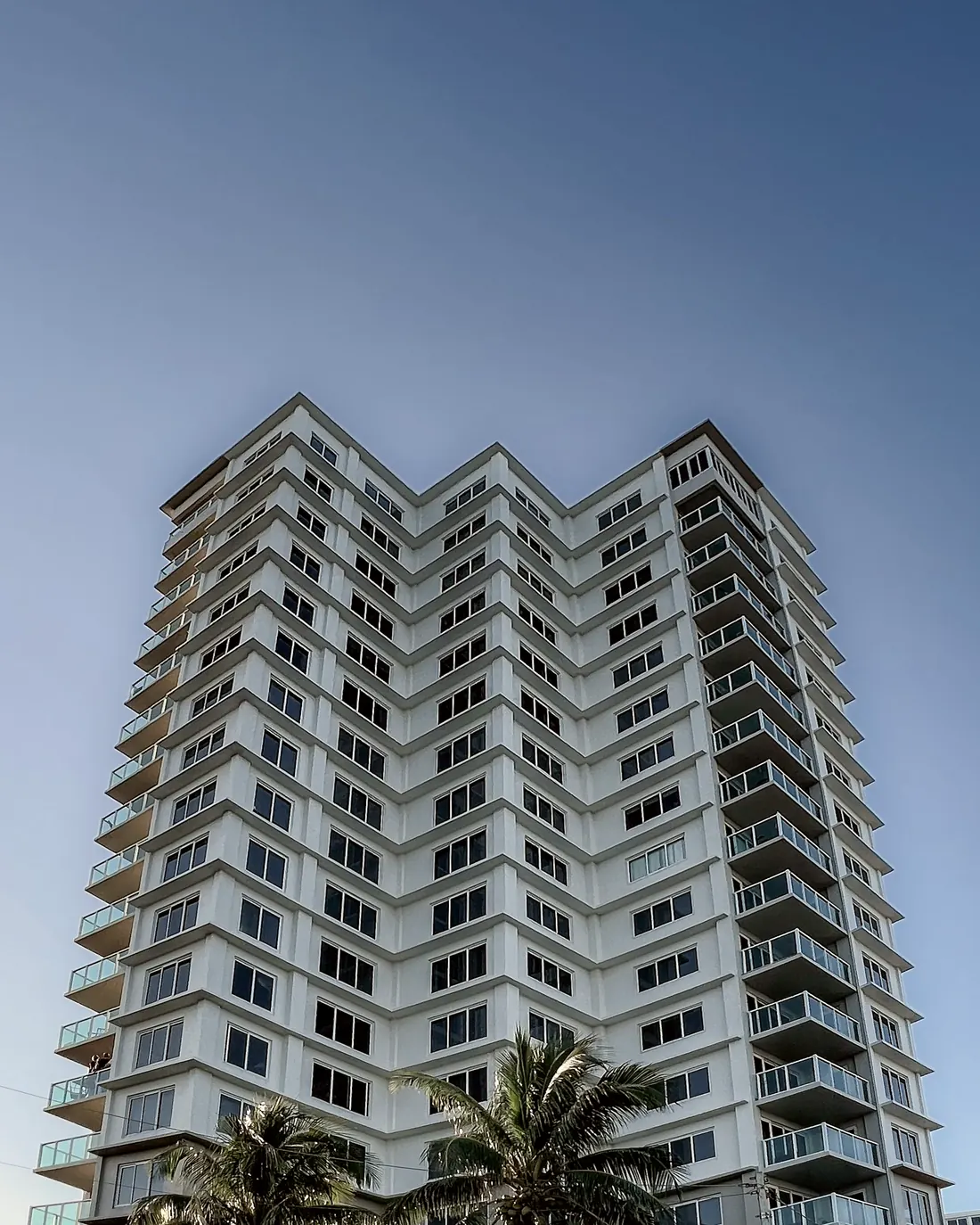 Torre residencial de gran altura al atardecer, vista desde la base con palmeras — referencia del penthouse Vista Sur en San Isidro